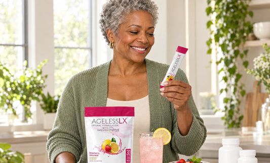 Woman in her late 50s reading an AgelessLX Strawberry Lemonade stick pack at a kitchen island with the AgelessLX pouch and unbranded supplement bottles